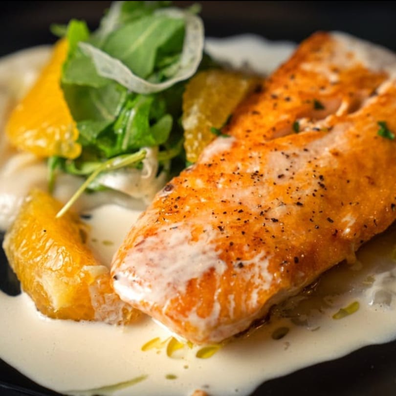 Favio's Trattoria's salmon dish with creamy sauce, orange slices, and arugula on a black plate.