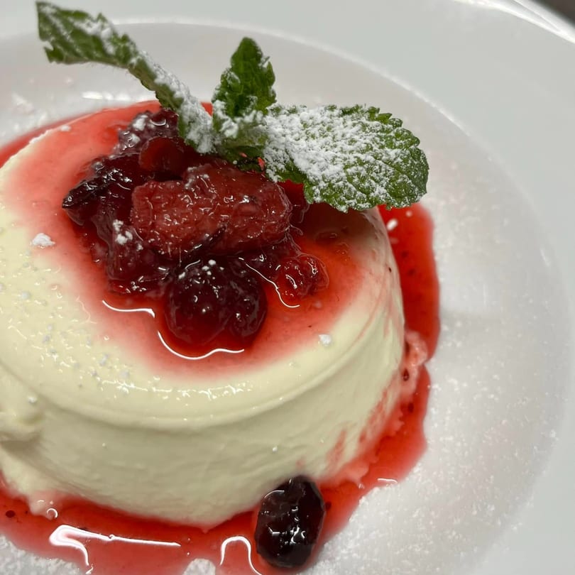 Favio's Trattoria's panna cotta dessert with berry compote, powdered sugar, and mint garnish.
