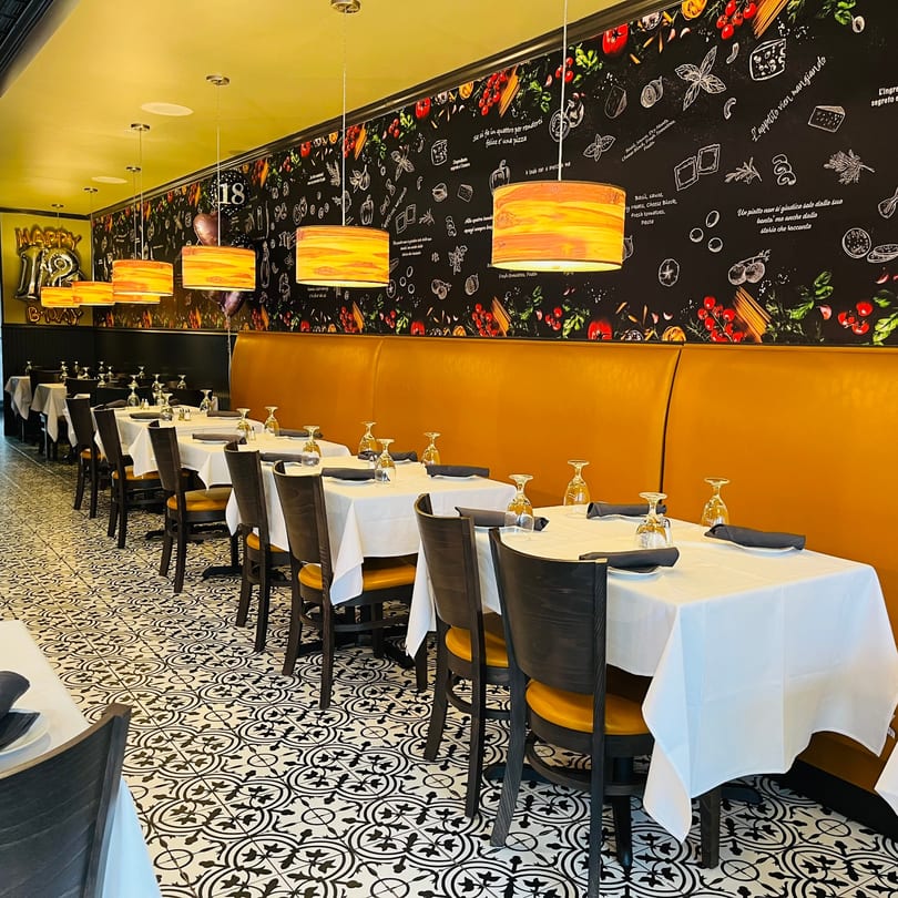 Favio's Trattoria's dining room with yellow booths, black and white patterned floor, and Italian-themed wall art.